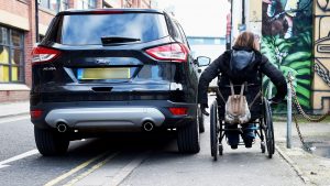 wheelchair user trying to get round car parked on pavement